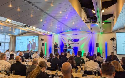 POSY OutputForum 2024 Veranstaltung Zwei Moderatoren stehen auf der Bühne während des POSY OutputForum 2024 mit Publikum im Hintergrund.